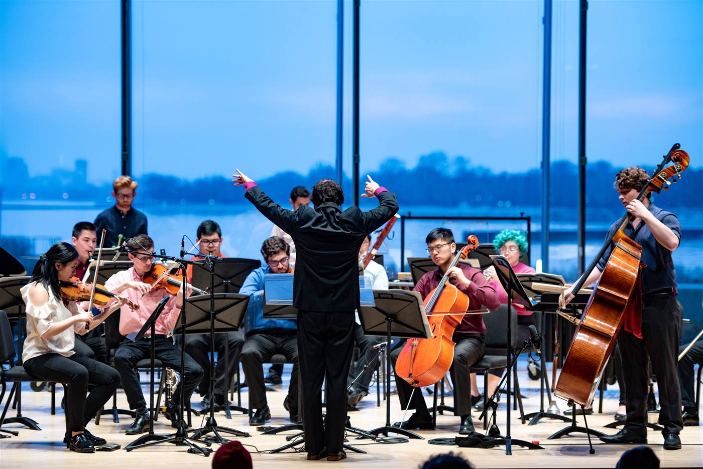 A student orchestra performing in front of windows onto the lake